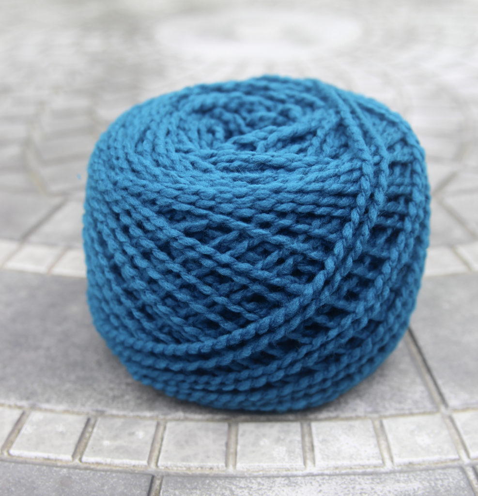 A cake of nubbly textured yarn in a teal color sits on a ceramic table.