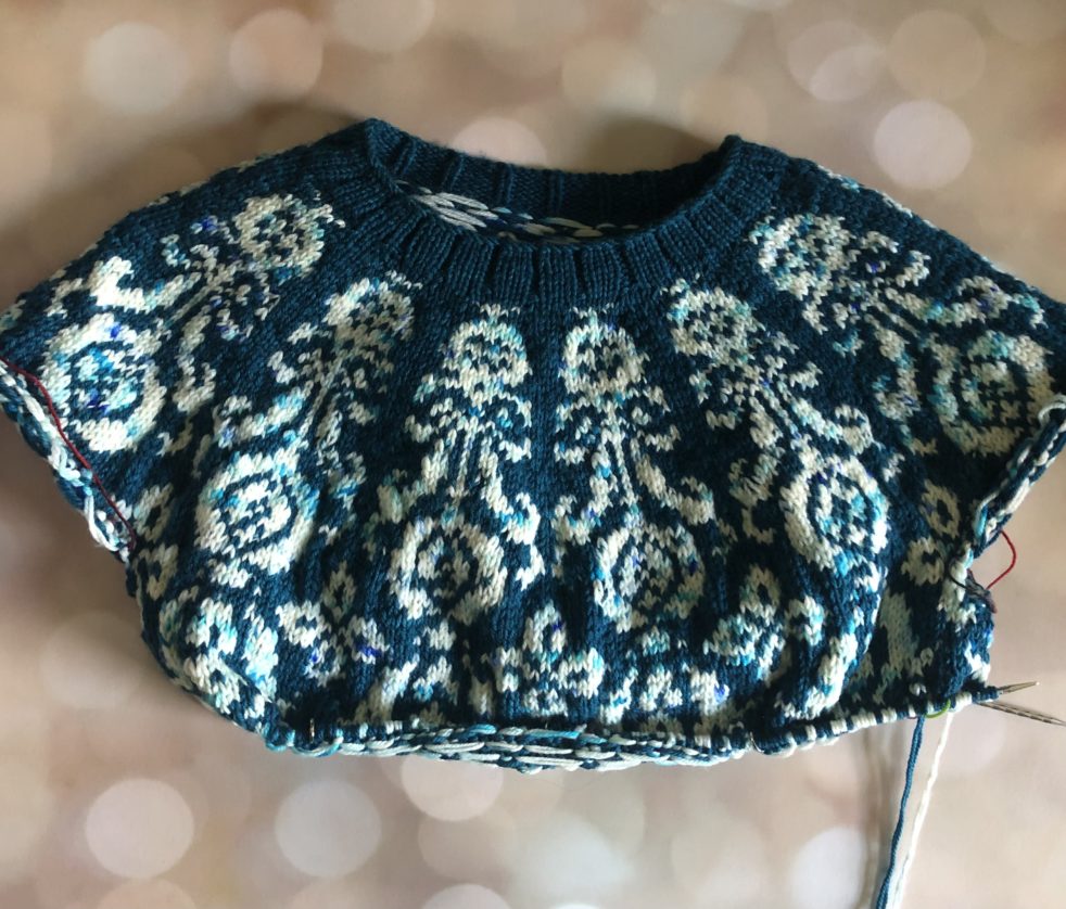 A teal sweater featuring a botanical colorwork design in a speckled white yarn.