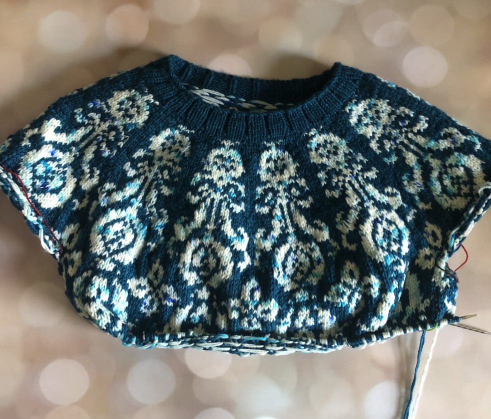 A teal sweater featuring a botanical colorwork design in a speckled white yarn.