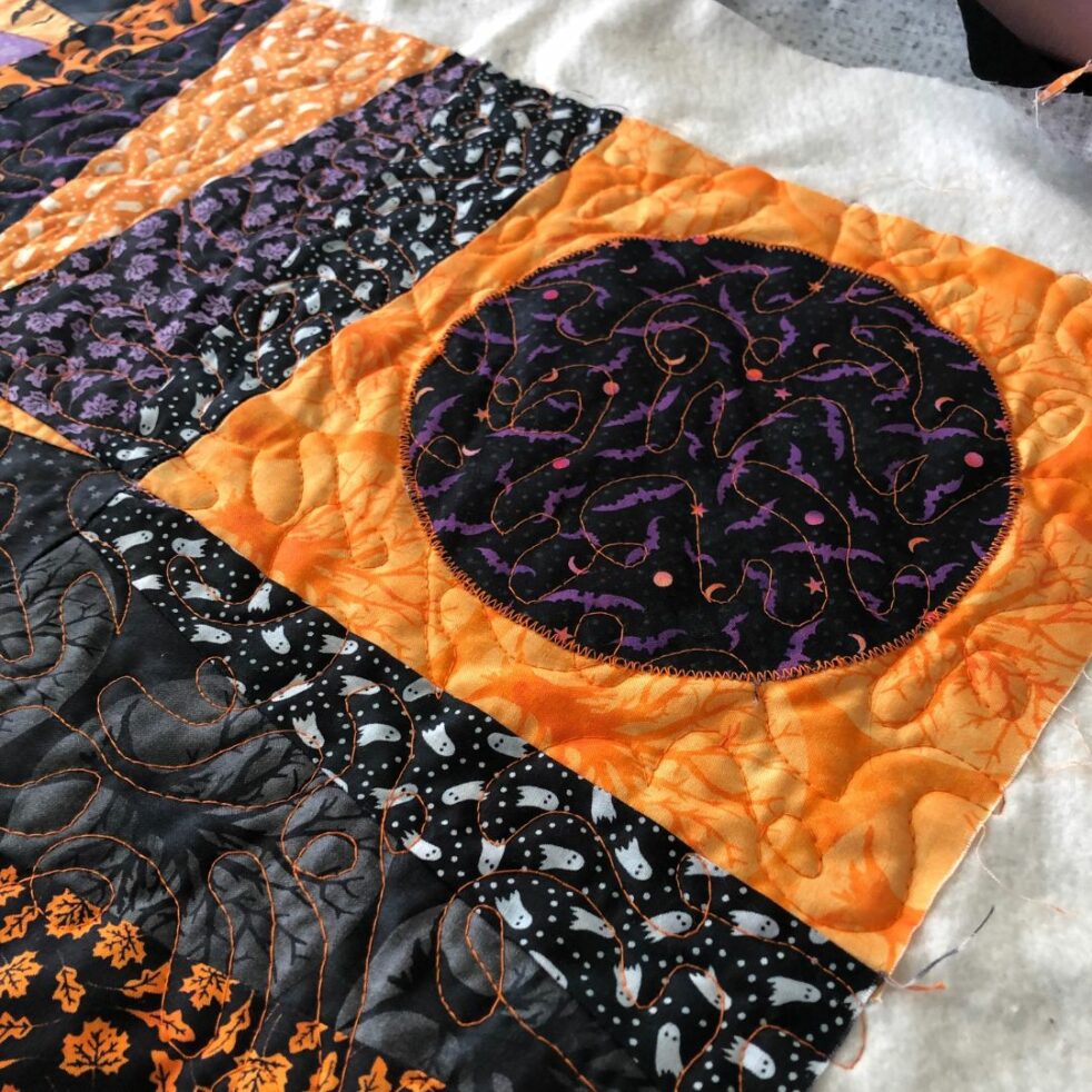 A quilt in Halloween fabrics in oranges, blacks and purples with meandering orange free motion quilting lines.