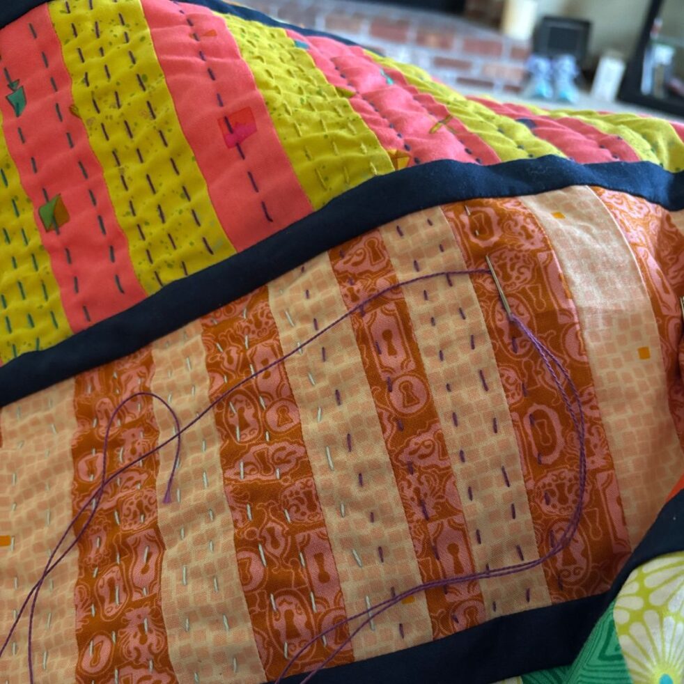 A brightly colored quilt featuring tiny hand stitches, called big stitch quilting.