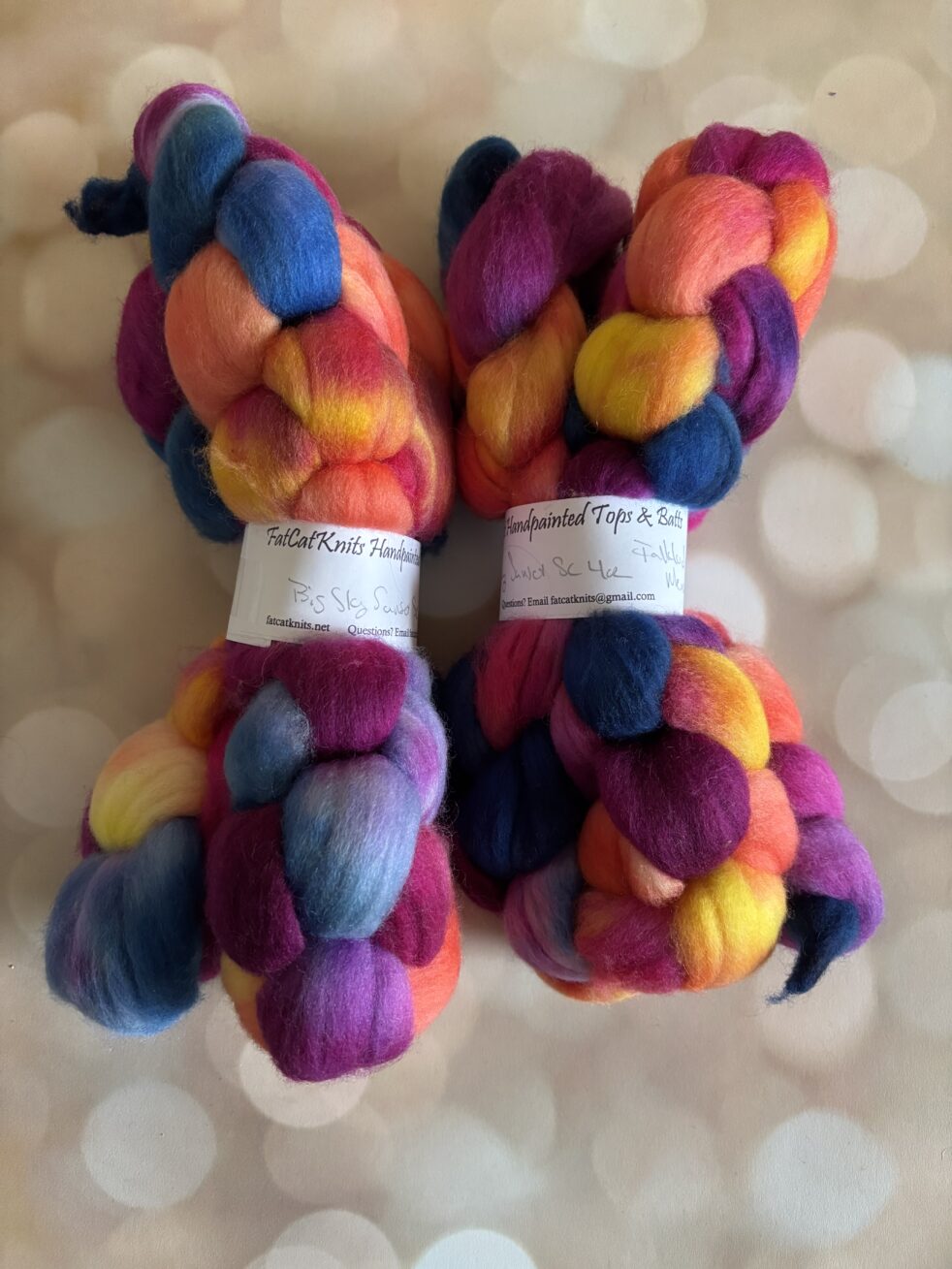 Two braids of fluffy wool fiber waiting to be spun in blue, pink, red, purple and yellow.