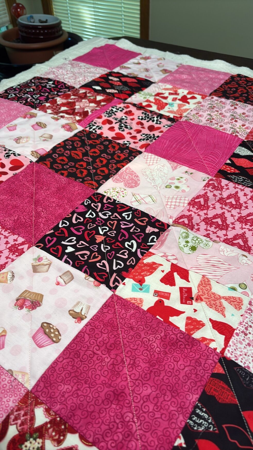 A scrappy patchwork quilt featuring squares of red, black, white and pink fabrics in Valentine’s Day themes.